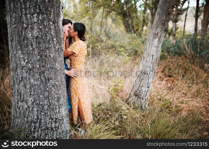 Two women kissing in the woods with dresses