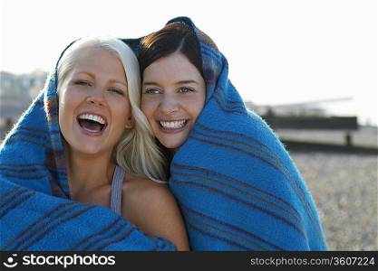 Two women laughing covered under blanket, portrait