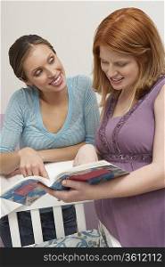 Two women looking at book by cradle
