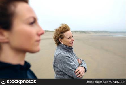 Two women looking at sea on the beach in autumn. Selective focus on woman in background. Two women looking at sea