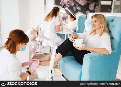 Two women on pedicure procedure in beauty salon. Professional beauticians and female customers, toenail care in spa studio. Two women on pedicure procedure in beauty salon