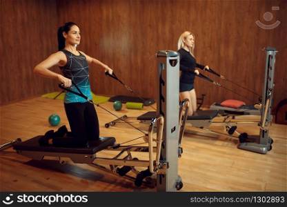 Two women on pilates training on exercise machine in gym, flexibility. Fitness workuot in sport club. Athletic female person, aerobics indoor, body stretching. Two women on pilates training in gym, flexibility