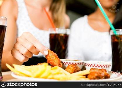 Two women - one is African American - eating chicken wings and drinking soda in a fast food diner; focus on the meal