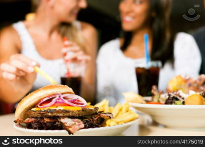 Two women - one is African American - eating hamburger and drinking soda in a fast food diner; focus on the meal