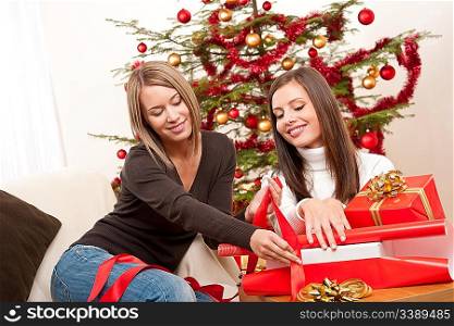 Two women packing Christmas present in front of tree