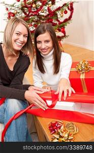 Two women packing Christmas present in front of tree