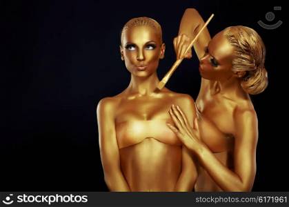 Two women painted in gold paint.