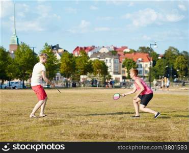 Two women play summer game in the park in the afternoon sunlight, city on background