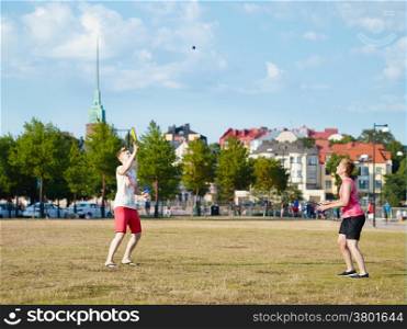 Two women play summer game in the park in the afternoon sunlight, city on background