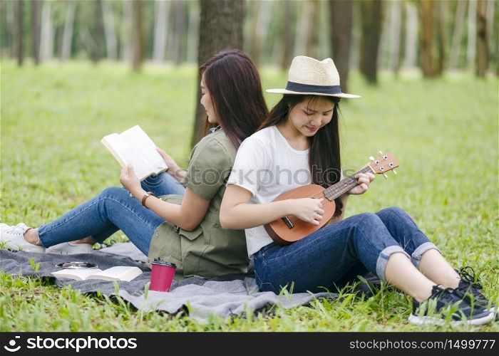 Two women playing ukulele and reading book together in the woods