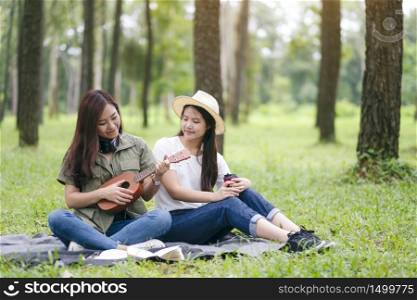Two women playing ukulele while sitting together in the woods