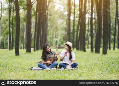 Two women playing ukulele while sitting together in the woods