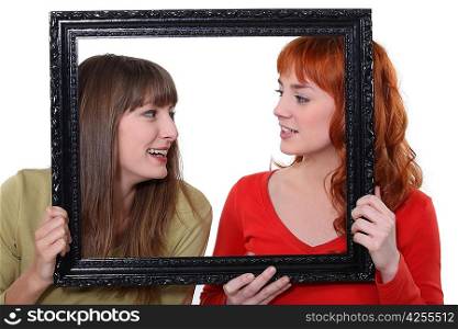 Two women poking heads though empty picture frame