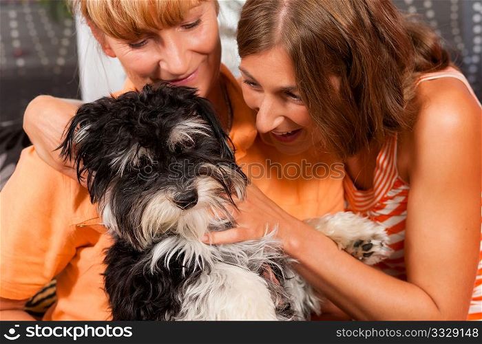 Two women ? presumably mother and daughter ? playing with a dog in her home