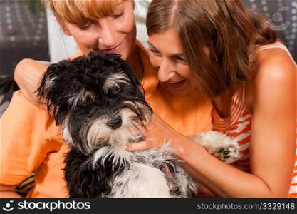 Two women ? presumably mother and daughter ? playing with a dog in her home