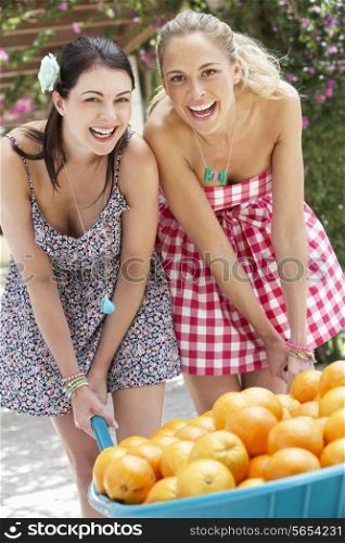 Two Women Pushing Wheelbarrow Filled With Oranges
