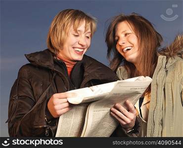 Two women reading newspaper, laughing