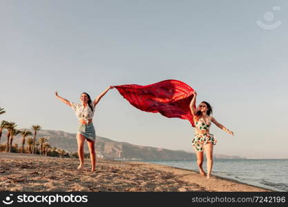 Two women running and holding scarf on wave relax and happy on beach