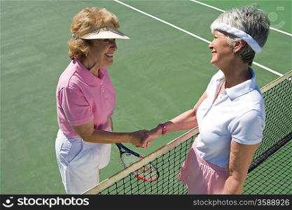 Two women shaking hands over tennis net