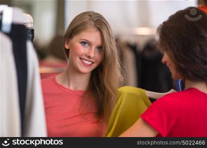 Two Women shopping choosing dresses. Beautiful young shoppers in clothing store.