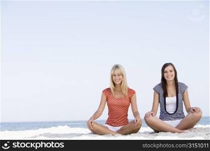 Two women sitting and meditating on a beach