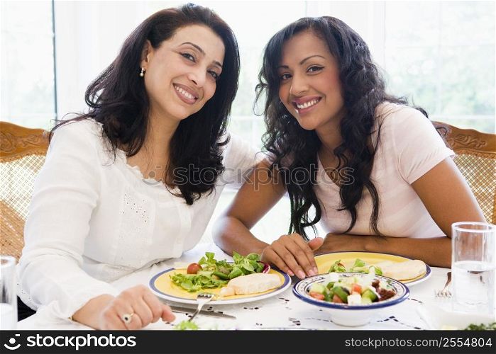 Two women sitting at dinner table smiling (high key)