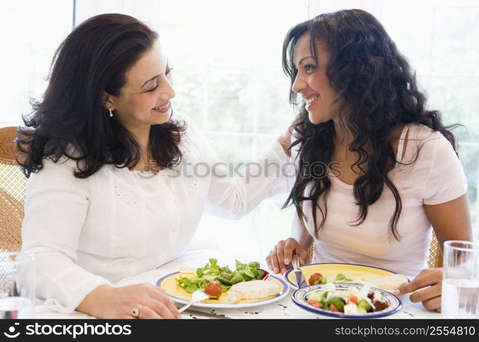 Two women sitting at dinner table smiling (high key)