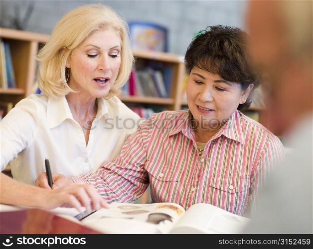 Two women sitting in library near a man with a book and notepad (selective focus)