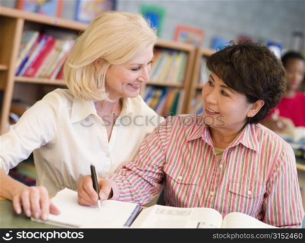 Two women sitting in library with a book and notepad (selective focus)