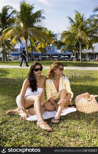 Two women sitting on blanket on grass