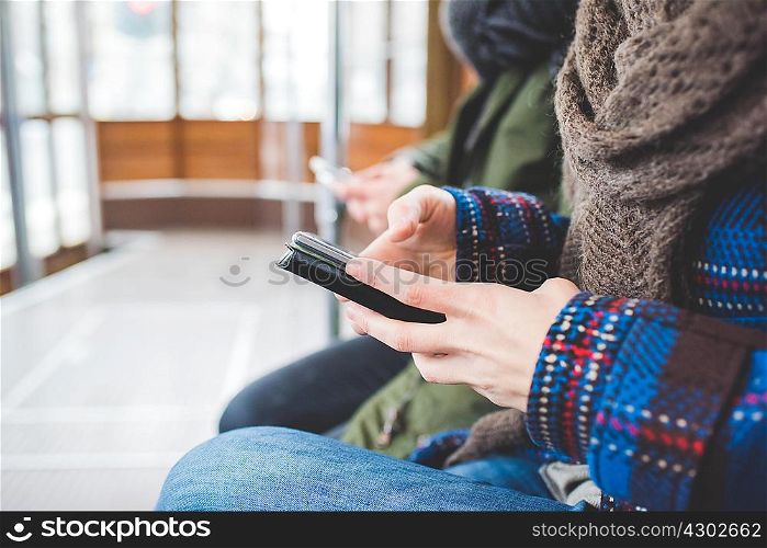 Two women sitting on cable car, using smartphones, mid section