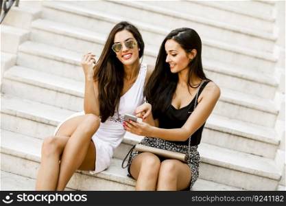 Two women sitting on the stairs outside and using mobile phone