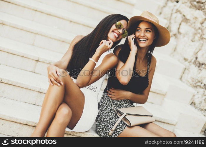 Two women sitting on the stairs outside and using mobile phone