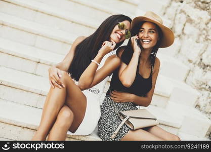 Two women sitting on the stairs outside and using mobile phone