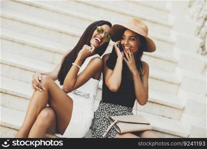 Two women sitting on the stairs outside and using mobile phone