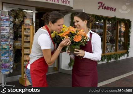 Two women smell flowers outside their flower shop
