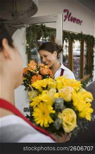 Two women smell flowers outside their flower shop