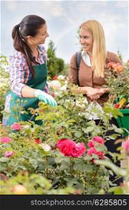 Two women talking about plants roses in garden center smiling