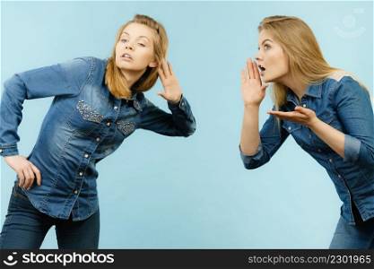 Two women talking gossip, telling tales, girls talk having fun wearing jeans outfit.. Two women telling tales, rumors gossip