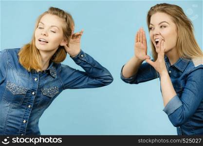 Two women talking gossip, telling tales, girls talk having fun wearing jeans outfit.. Two women telling tales, rumors gossip