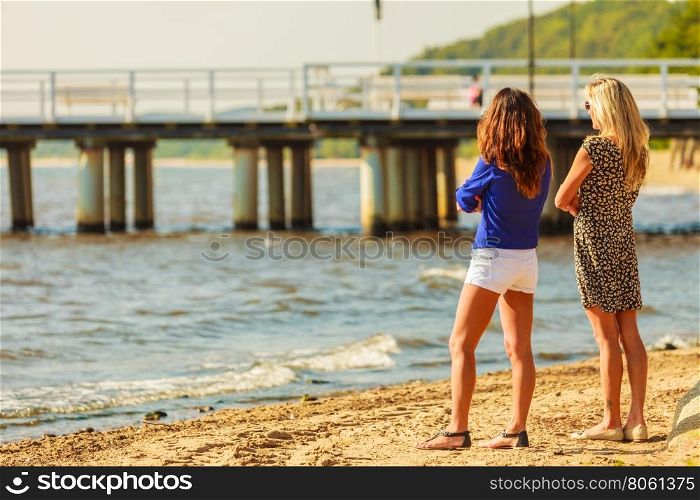 Two women talking resting on beach.. Relaxation and leisure. Attractive mid aged women talking resting on beach. Female tourists relax near to water place on nature.