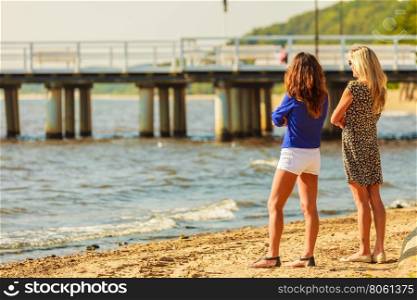 Two women talking resting on beach.. Relaxation and leisure. Attractive mid aged women talking resting on beach. Female tourists relax near to water place on nature.