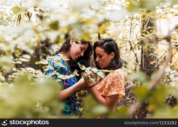 Two women touching their hands surrounded by forest plants