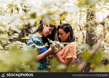 Two women touching their hands surrounded by forest plants