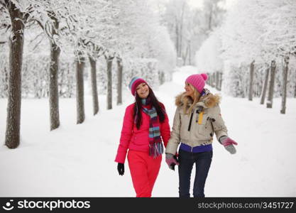 two women walk by winter alley snow trees on background