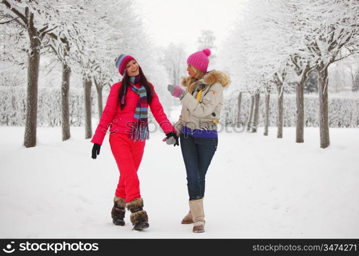 two women walk by winter alley snow trees on background