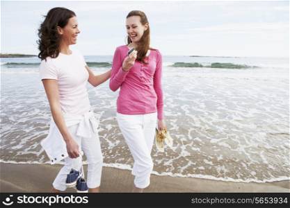 Two Women Walking Along Beach Looking At Mobile Phone