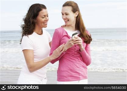 Two Women Walking Along Beach Looking At Mobile Phone