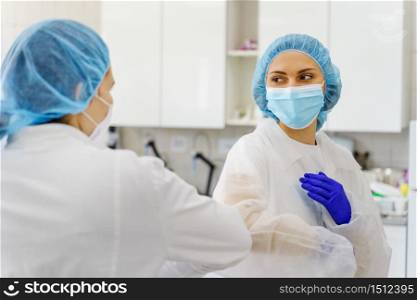 Two women wearing protective equipment bouffant mob cap and protective mask - Elbow bump greeting at hospital or laboratory new normal due to corona virus pandemic spread - support and safety concept