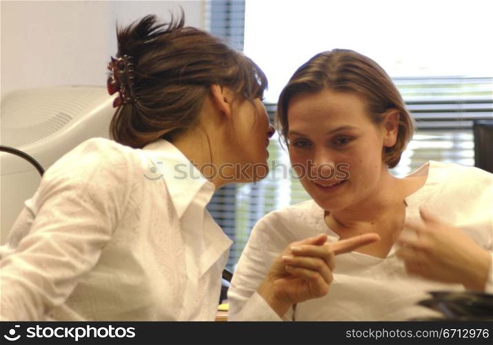 two women whispering in an office